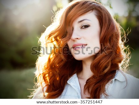 Emotional portrait of happy beautiful woman with red curly hair and natural makeup enjoying her life in nature. Soft sunny colors. Outdoor shot. Copyspace.