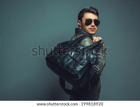 Portrait of young handsome fashion man with leather bag wearing sunglasses and leather jacket. Close up. Copy-space. Studio shot
