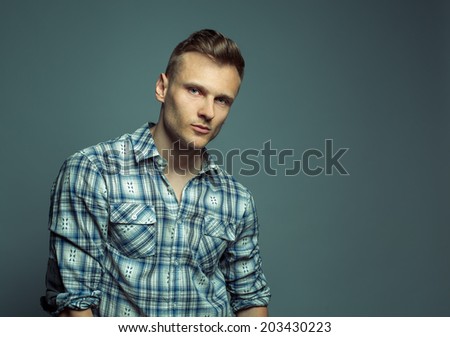 Fashion portrait of young handsome blond man in shirt poses over grey background
