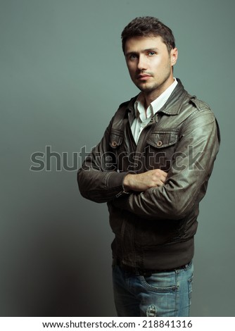 Male beauty concept. Portrait of a fashionable young man with stylish haircut wearing jeans and leather jacket,  posing over gray background. Perfect hair & skin. Hipster style. Close up. Copy-space