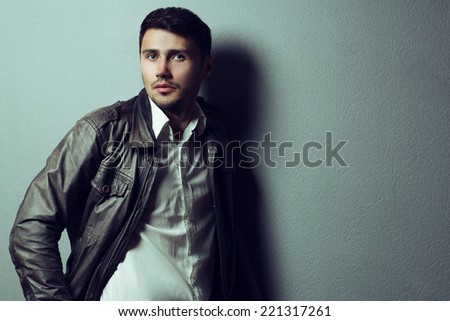 Male beauty concept. Portrait of fashionable young man with stylish haircut wearing leather jacket and white shirt, over gray background. Perfect hair & skin. Hipster style. Copy-space. Studio shot
