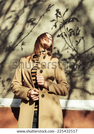 Seductive glamorous brunette wearing stylish clothes posing outside over wall with beautiful shadows