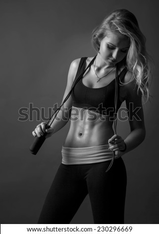 Sport  blond woman with skipping rope showing her well trained body and strong abs. Black and White.