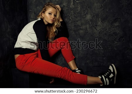 Beautiful girl model. Fashion portrait of stylish blond girl in trendy red pants, black and white sweater and sneakers.  Smoky eyes make up.