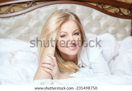 Beautiful young and sexy sensual blond glamorous girl in luxurious bed on white blanket. Smiling and looking at camera.