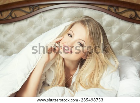 Good morning concept. Beautiful young woman in luxury comfortable bad under white blanket and sheet. Smiling and looking and camera.