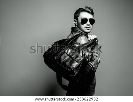 Fashion portrait of handsome man in leather, sunglasses, trendy jacket and black modern bag. Studio shot. Close up.
