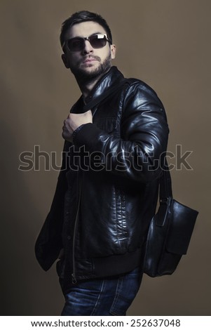 Fashion portrait of handsome young man in trendy casual leather jacket  and jeans with leather black bag.