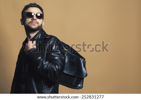 Fashion portrait of handsome young man with in trendy casual leather jacket, trendy sunglasses  and man\'s bag.