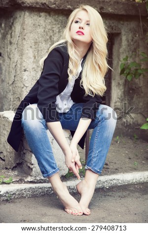 Sexy  blond woman in trendy jeans, white shirt and black jacket posing in the street barefoot.