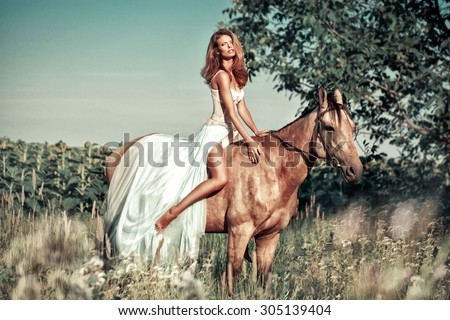Beautiful young lady wearing in long dress  riding a horse at sunny summer day. Vintage toned photo.