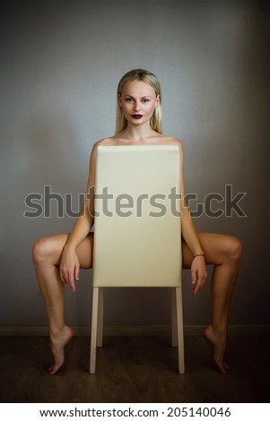 Emotive portrait of nude beautiful woman with long blonde hair on the chair.