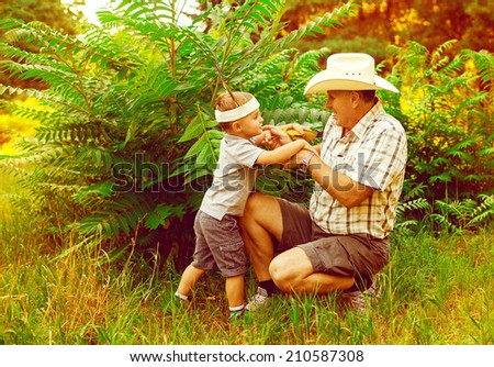 Father and son are playing in nature. Indian and cowboy together on the grass