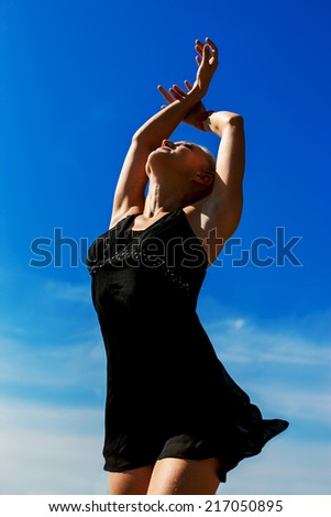 Beautiful young dancer performing yoga-dance outdoors with blue sky and clouds in the background.