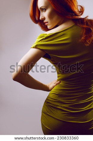 Emotive portrait of a fashionable model with red (ginger) curly hair and natural make-up posing over grey background. Perfect skin. Studio shot. Sexy green dress