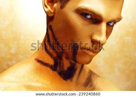 Dramatic art portrait of man in bronze paint on his body and gold makeup.  Close up portrait of a man with the trace from women\'s hands