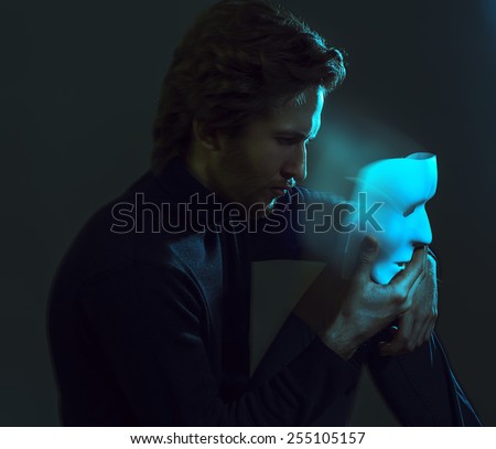 arty portrait of a man with mask, holding and looking at venetian mask (volto bianco), thinking about the changes. Conception of a choice in this life