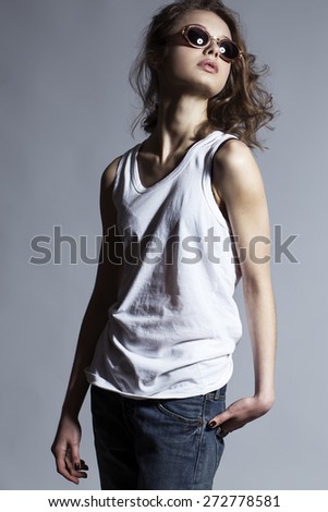 High fashion look. Portrait of a fashionable model with natural make up and perfect skin, dressed in men\'s jeans, white shirt and stylish round glasses.  Studio shot
