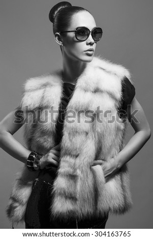 Sexy Beauty Girl with natural  Make up.  Fashion Brunette Portrait of a girl dressed in fur coat and black sunglasses posing on a grey background. Retro style. Monochrome (black and white)  photo