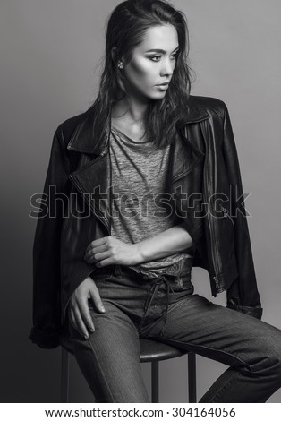 Portrait of a fashionable model with natural make up and perfect skin, dressed in men\'s jeans, grey shirt, black jacket and sneakers.Studio shot. High fashion look.Monochrome (black and white)  photo
