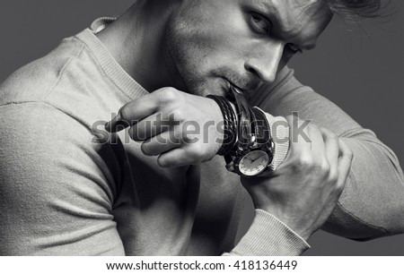 Advertising wrist watch concept. Beautiful (handsome) muscular male model with perfect body in grey jumper. He bites and unfastens the bracelet from the clock. Street style. monochrome studio shot
