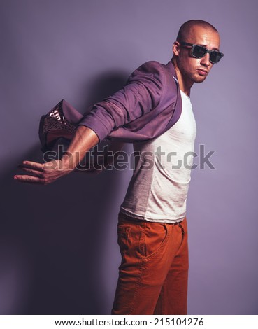 Young handsome man in trendy glasses, purple jacket, white undervest and orange briefs over purple background. Studio shot. Copy space.