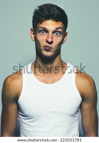 Emotive portrait of a funny handsome young man in white undershirt posing over grey background. Studio shot. Close-up