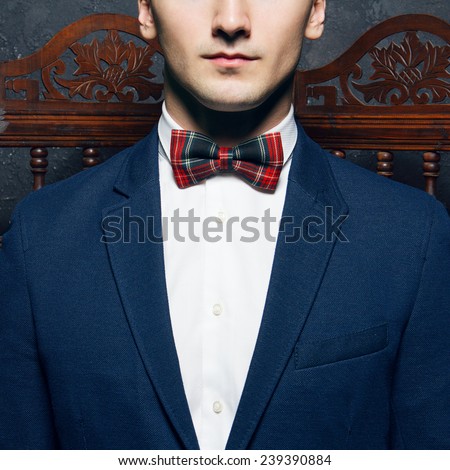 English gentleman beauty concept. Half-face portrait of young man in blue jacket, Scottish bow tie and white shirt posing over vintage screen. Close up. Studio shot
