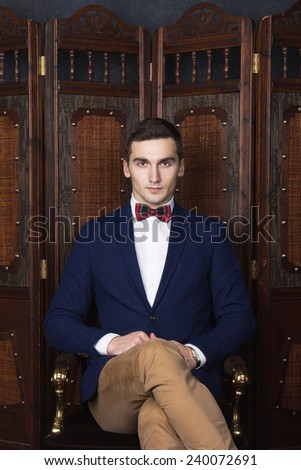 English gentleman beauty concept. Portrait of young and handsome man in blue jacket, Scottish bow tie and white shirt posing over vintage screen. Close up. Studio shot