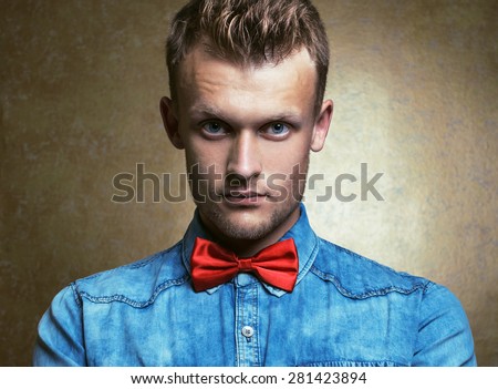 Portrait of a hipster young and handsome man in blue jeans shirt and red bow-tie over vintage background. Pensive emotive face. Close up. Studio shot