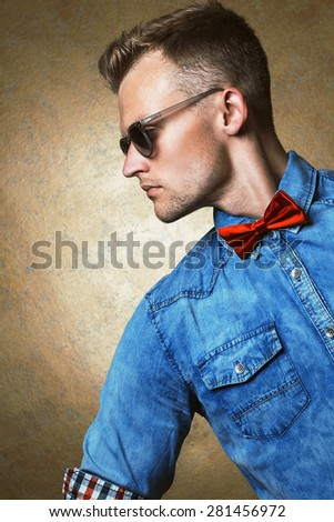 Sunglasses concept. Portrait of a hipster young and handsome man in sunglasses, blue jeans shirt and red bow-tie over vintage background. Close up. Studio shot