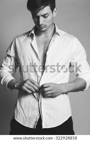 Male beauty concept. Portrait of fashionable young man with stylish haircut wearing white shirt & posing over grey background. Studio shot
