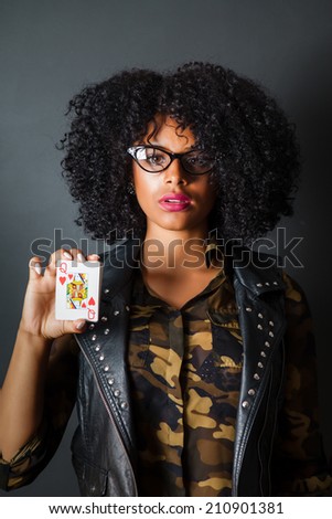 Hipster girl with afro wearing camouflage and leather holding queen of hearts card