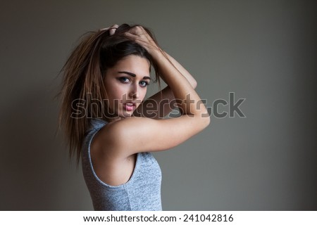 Portrait of gorgeous, muscular young woman with long brown hair and blue eyes. Posing in studio, wearing fashionable clothing.  Holding tousled hair above head. Ombre hair.