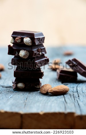 Stack of chocolate pieces with nuts on rustic wooden board, selective focus