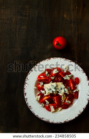 Salad with tomatoes and blue cheese on rustic wooden texture.Top view