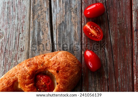 Top view of Focaccia with tomatoes on rustic wooden texture.