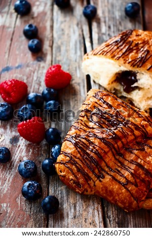 freshly baked chocolate croissants with berries for breakfast over rustic wooden texture. Selective focus.