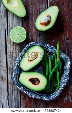 Top view of ripe halved avocados and green beans  on vintage metal plate - healthy food, diet or cooking concept.