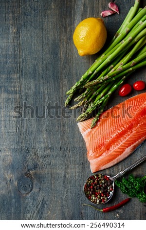 Portion of salmon fillet with asparagus and aromatic herbs, spices and vegetables over wood - healthy food, diet or cooking concept. Top view.