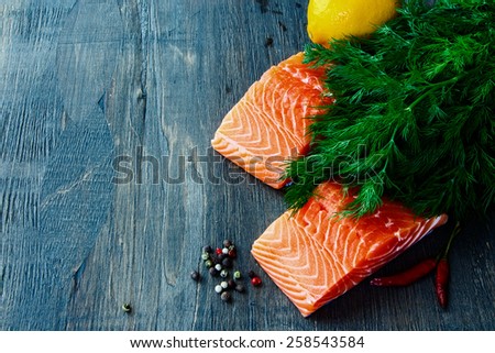 Fresh salmon fillet with aromatic herbs and spices over dark wooden texture - healthy food, diet or cooking concept.