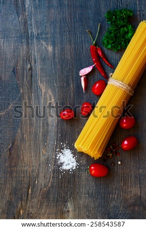 Top view of spaghetti and tomatoes with herbs over rustic and vintage wooden texture.