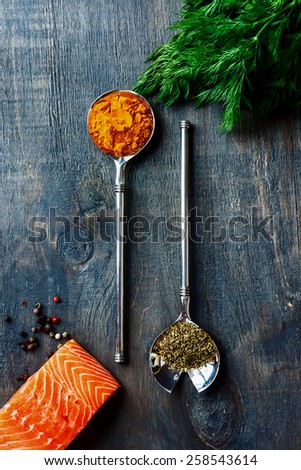 Top view of salmon fillet with aromatic herbs and spices over dark wooden texture - healthy food, diet or cooking concept.