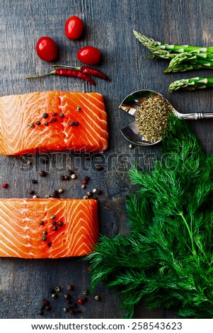 Delicious salmon fillet with asparagus and aromatic herbs, spices and vegetables over wood background- healthy food, diet or cooking concept. Top view.
