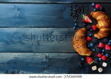 Top view of coffee, berries and fresh croissants for breakfast over wood. Background with space for text.