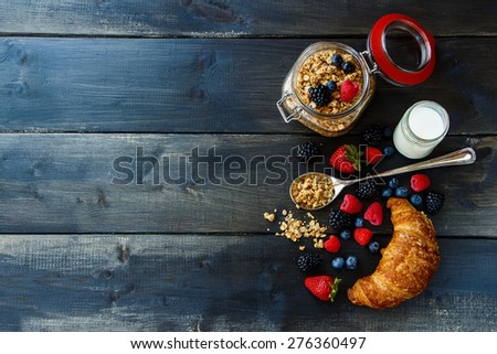 Croissant, fresh berries, yogurt and homemade granola in glass jar for breakfast on dark wooden table. Health and diet concept. Background with space for text.
