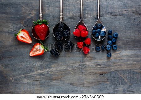 Top view of berries mixed (strawberries, raspberries, blueberries and blackberries) on vintage metal spoons over dark wood. Agriculture, Gardening, Harvest Concept. Background with space for text.