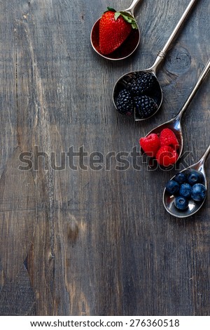 Berries mixed on vintage metal spoons over dark wooden board. Agriculture, Gardening, Harvest Concept. Background with space for text.
