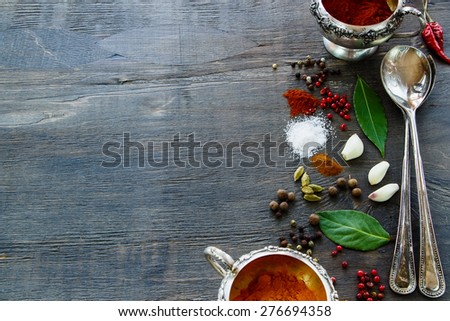 Old metal cups and spoons with spices selection on dark wooden table. Background with space for text.