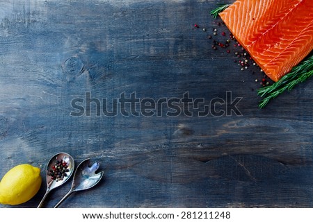 Delicious salmon fillet, aromatic spices and lemon on dark wooden background with space for text. Vegetarian food, health or cooking concept. Top view.
